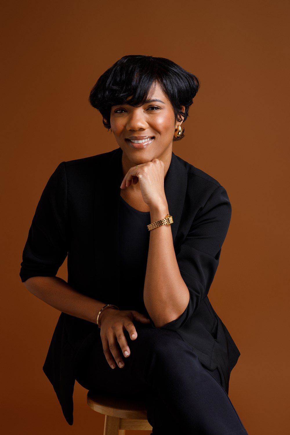 Crystal Mars-Noel, founder of Beyond Mars Consulting, seated against a warm rust backdrop